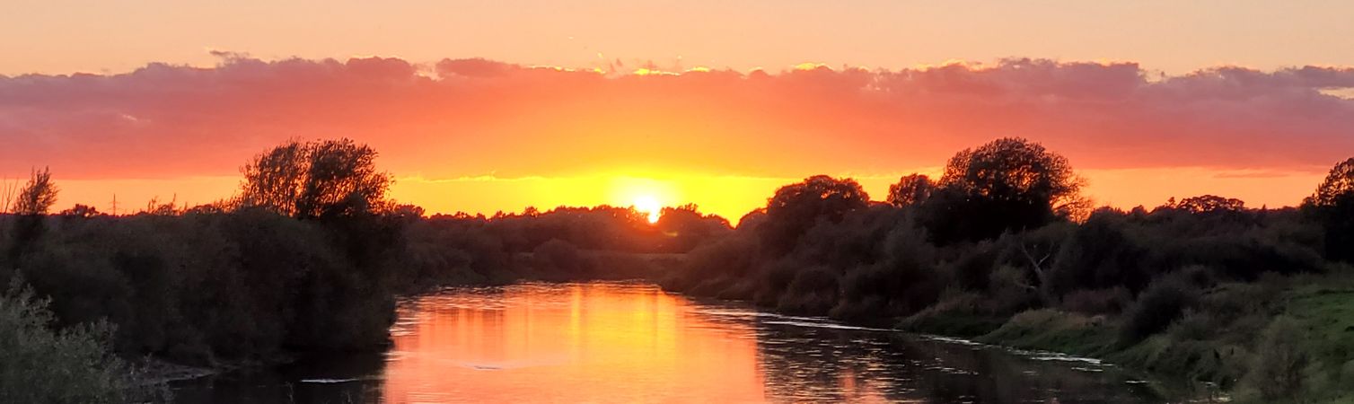 Sonnenuntergang Sonnenuntergang im Hintergrund; vorne ist ein Fluss mit Grün an beiden Uferseiten